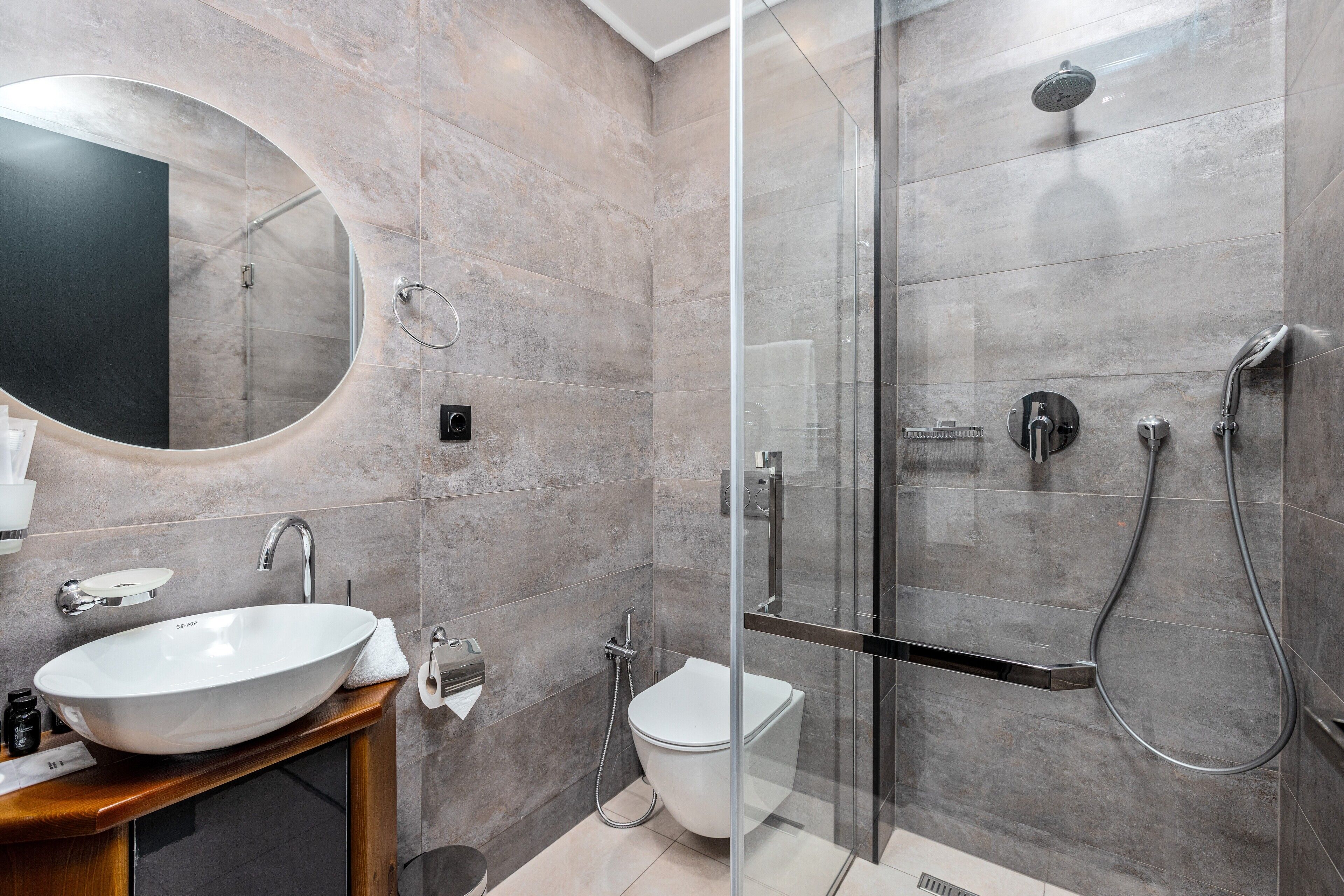A modern bathroom with a large oval mirror, a vessel sink, a glass-enclosed shower, and a toilet.