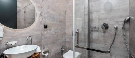 A modern bathroom with a large oval mirror, a vessel sink, a glass-enclosed shower, and a toilet.
