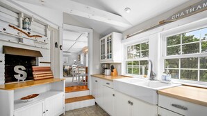 Une cuisine avec des meubles blancs, un plan de travail en bois et une fenêtre donnant sur des arbres.