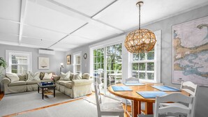 Un salon spacieux avec une grande fenêtre, une table ronde en bois et un lustre en rotin.