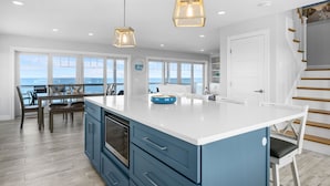 A spacious kitchen with a large island, wooden flooring, and a view of the ocean. - Oceanfront Cape Escape with Panoramic Bay Views (East Sandwich)