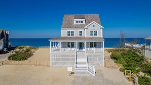 A two-story beach house with a covered porch and a staircase leading to the entrance. - Oceanfront Cape Escape with Panoramic Bay Views (East Sandwich)