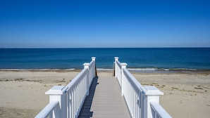 A wooden boardwalk leading to a beach with a clear blue sky. - Oceanfront Cape Escape with Panoramic Bay Views (East Sandwich)