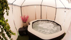 A hot tub inside a tent with a green floor and a potted plant with pink flowers. - Castelinho Solemar - Hot Spa (Praia Grande)