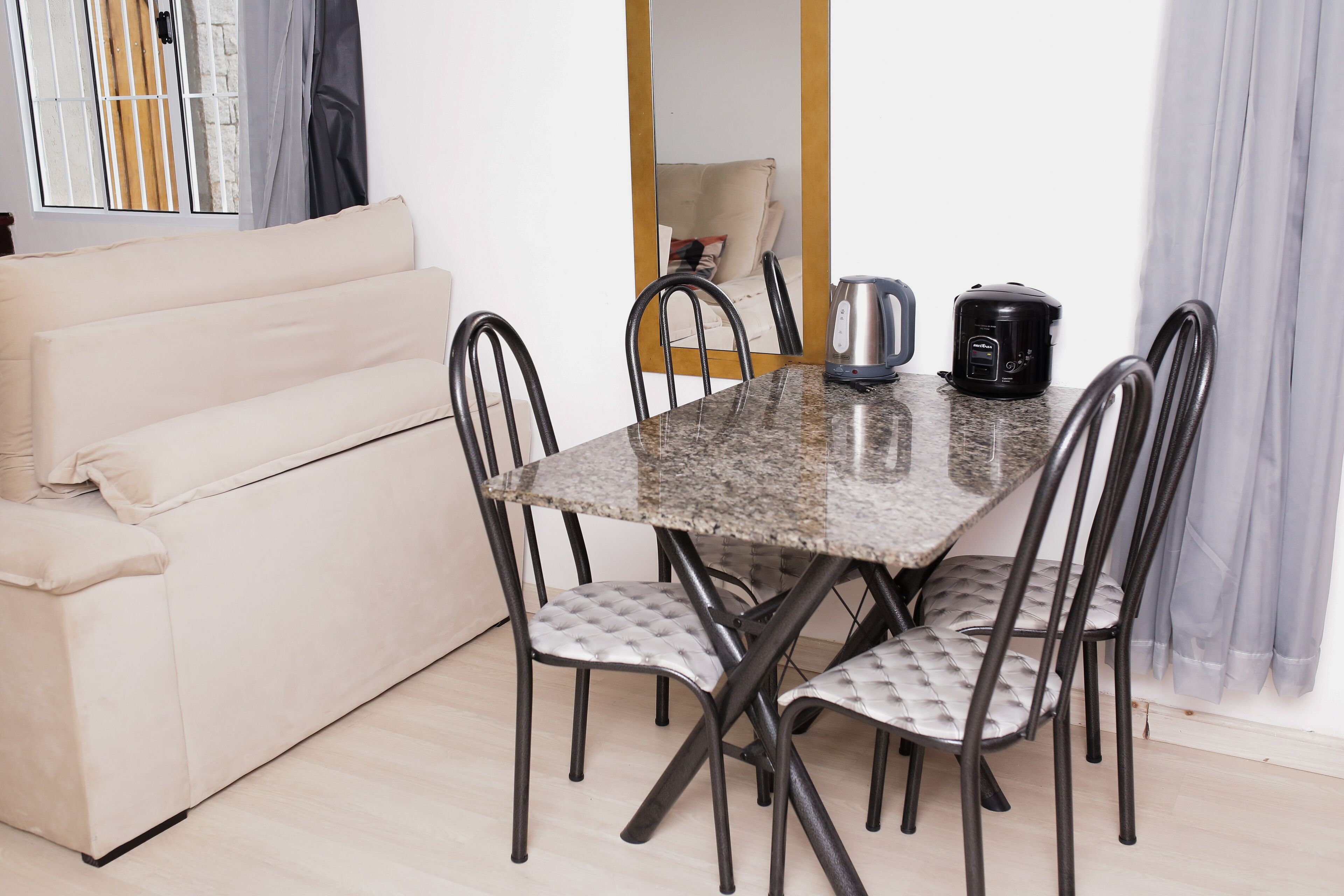Un coin repas comprenant une table en marbre, quatre chaises rembourrées, un canapé, une bouilloire et une machine à café.