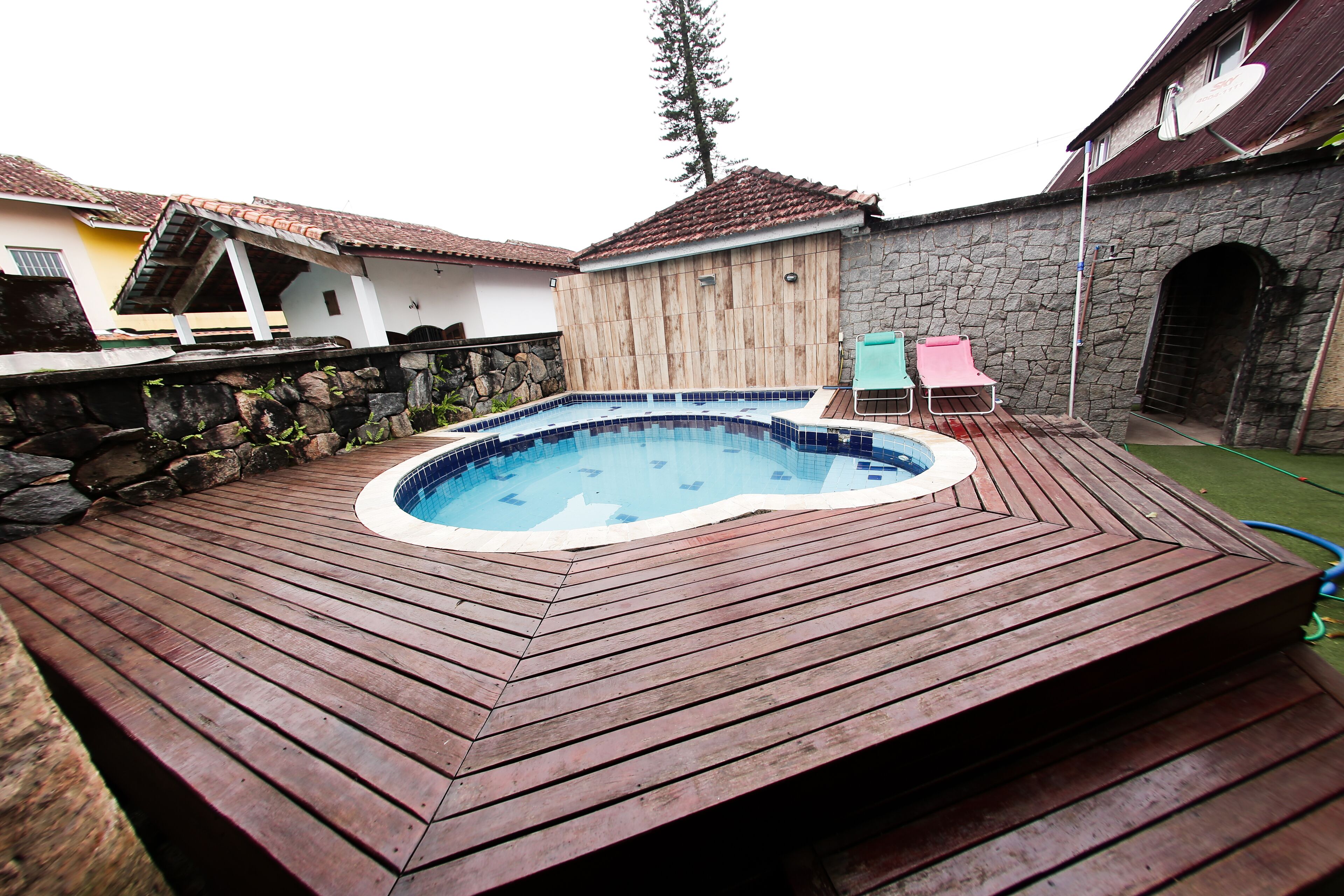 Una terraza de madera con un jacuzzi, un muro de piedra y un edificio de piedra al fondo.