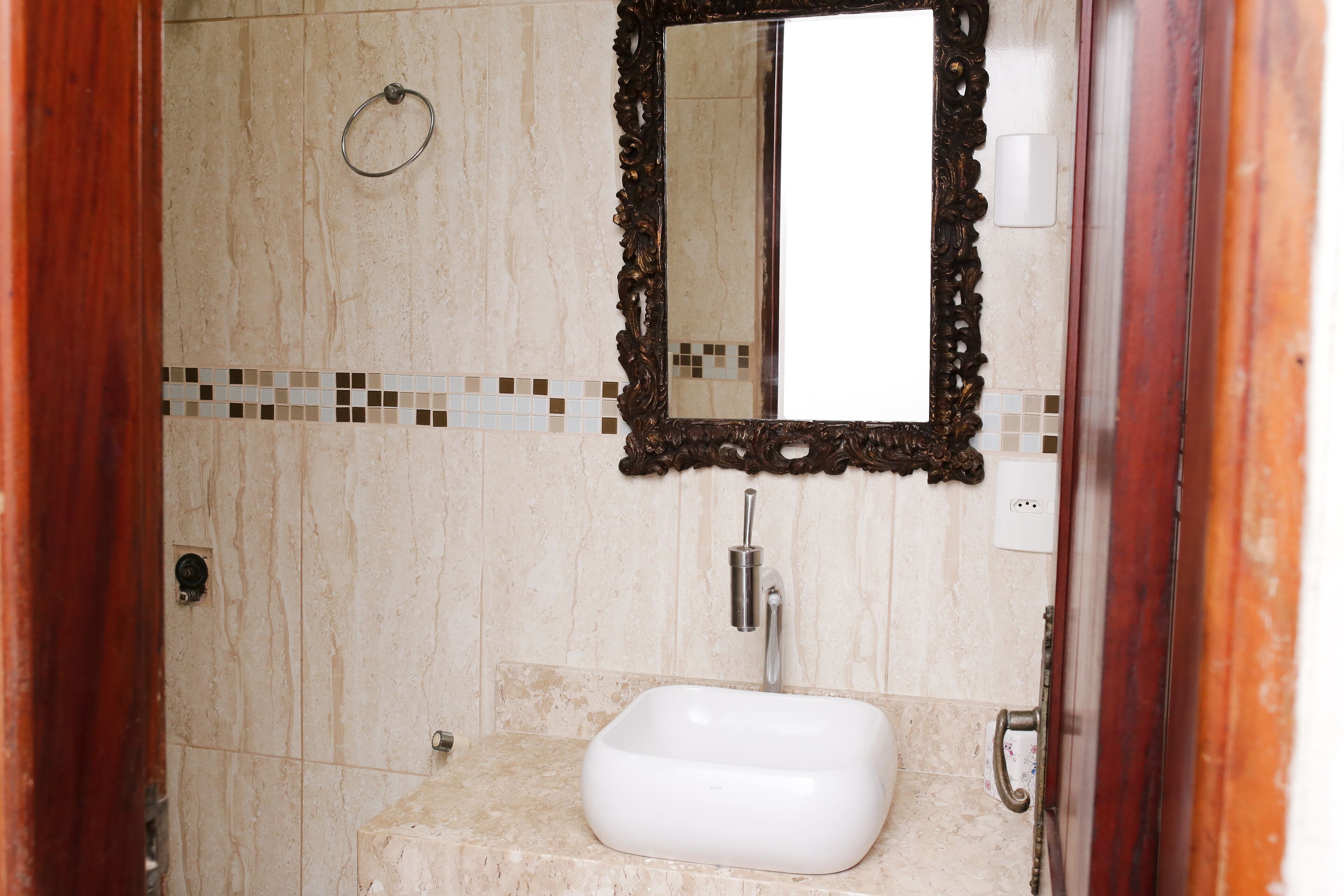 A bathroom with a white sink, a mirror with an ornate frame, and a tiled backsplash.