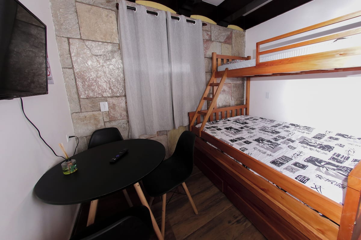A room with a bunk bed, a small table with chairs, a TV, and a curtain.