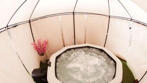 A hot tub inside a tent with a pump and a vase of pink flowers. - Castelinho Solemar - Hot Spa (Praia Grande)