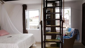 A bedroom with a bed, a wooden ladder, a window, and a chair with a blanket. - Castelinho Solemar - Hot Spa (Praia Grande)