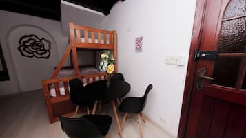 A room with a bunk bed, a small table with chairs, a vase with flowers, and a door with a frosted glass panel.
