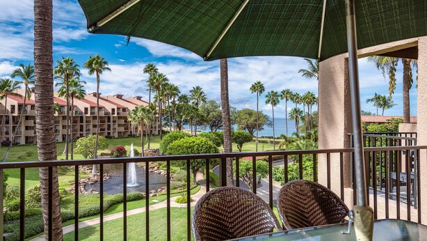 A balcony with wicker chairs, a table, and a large umbrella. - Kamaole Sands 1-403 - Ultimate getaway!  Spacious 2/2 with split AC, Large Lanai (Kihei)