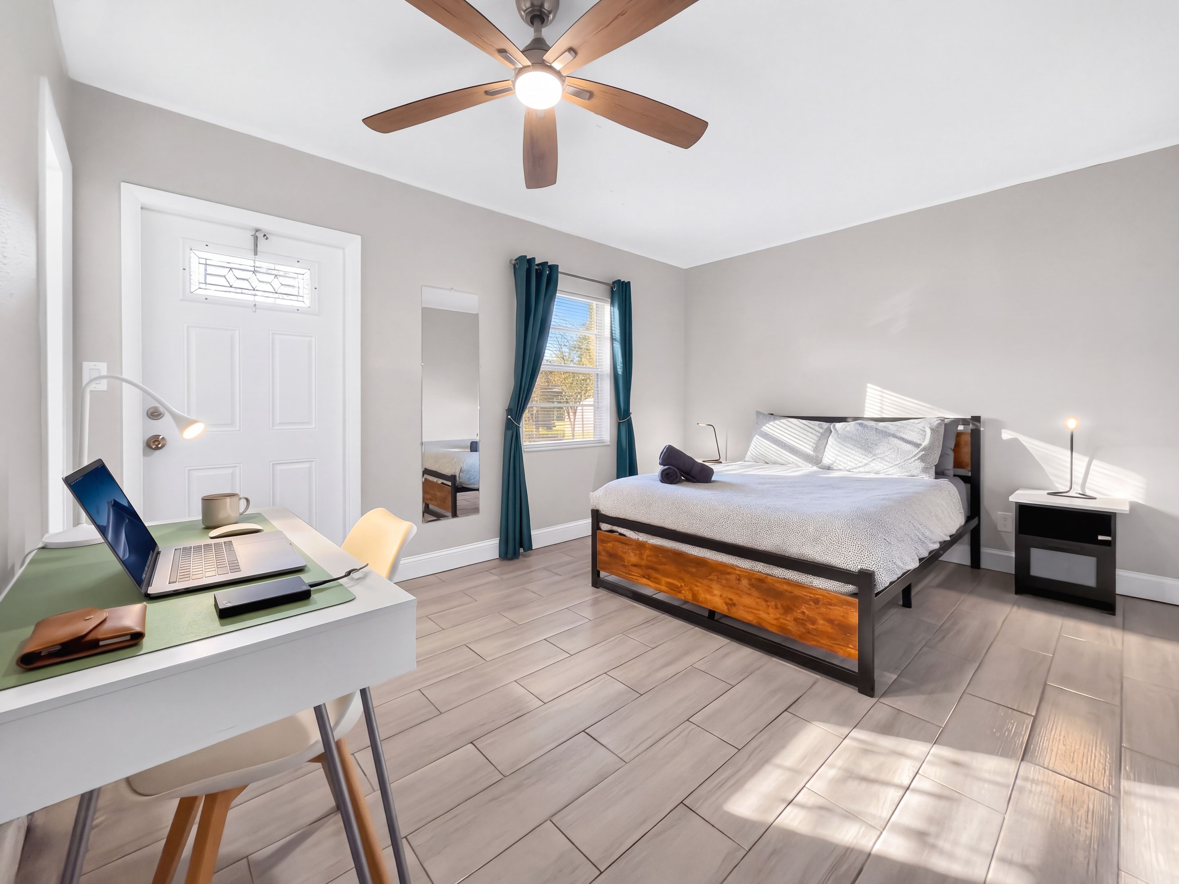 Une chambre à coucher comprenant un lit, une table de chevet, un bureau avec un ordinateur portable, une chaise et un ventilateur de plafond.
