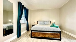 A bedroom with a bed, a mirror, curtains, and a nightstand.