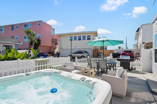 A backyard with a hot tub, outdoor furniture, a grill, and a white picket fence.