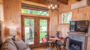 A cozy cabin interior with a sofa, a dining table with chairs, a fireplace, and a TV mounted above it.