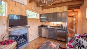 A cozy cabin interior with a fireplace, a television, a kitchen with modern appliances, and a comfortable seating area.