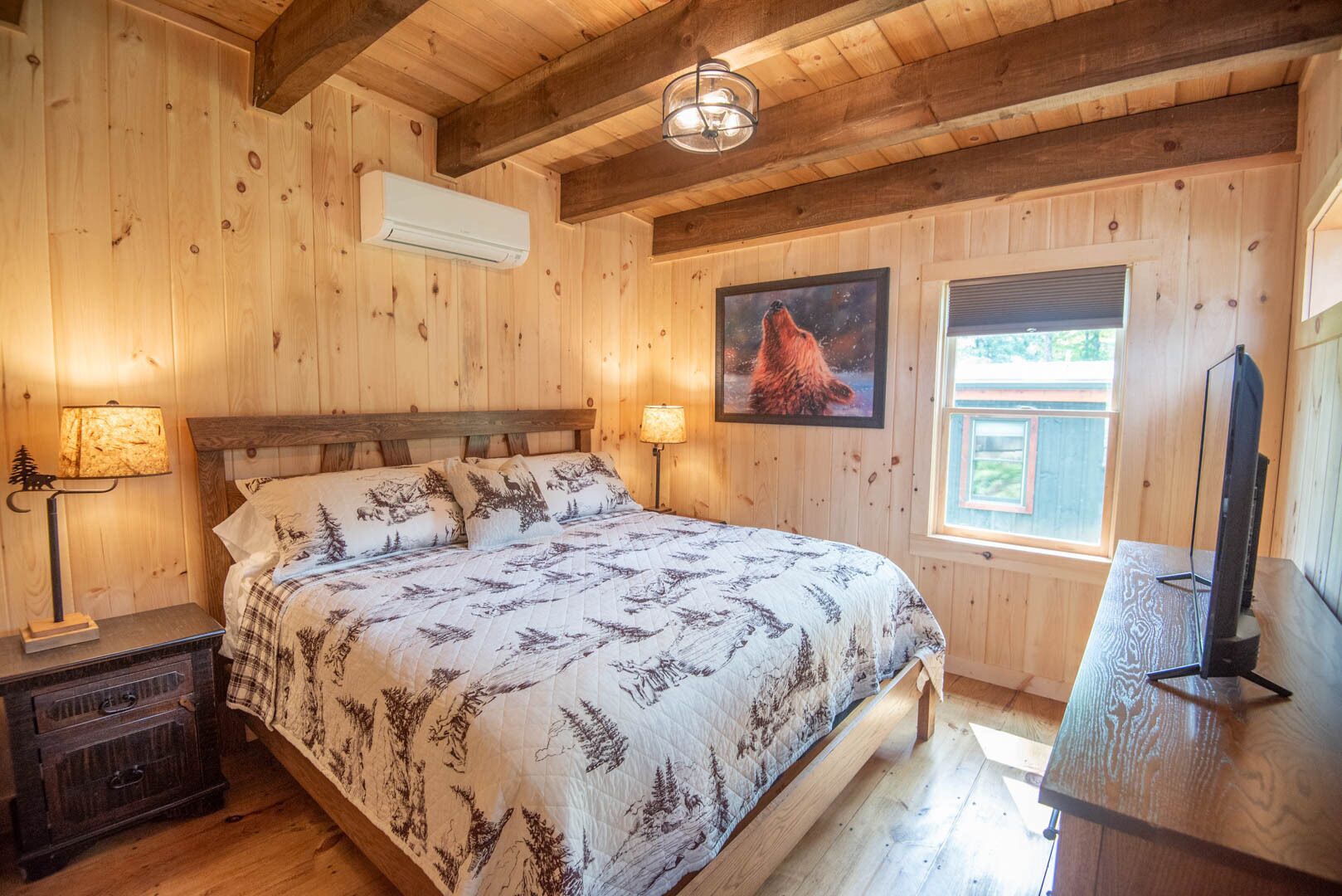 A wooden-paneled bedroom with a bed, two bedside lamps, a mounted TV, and a window with a view.