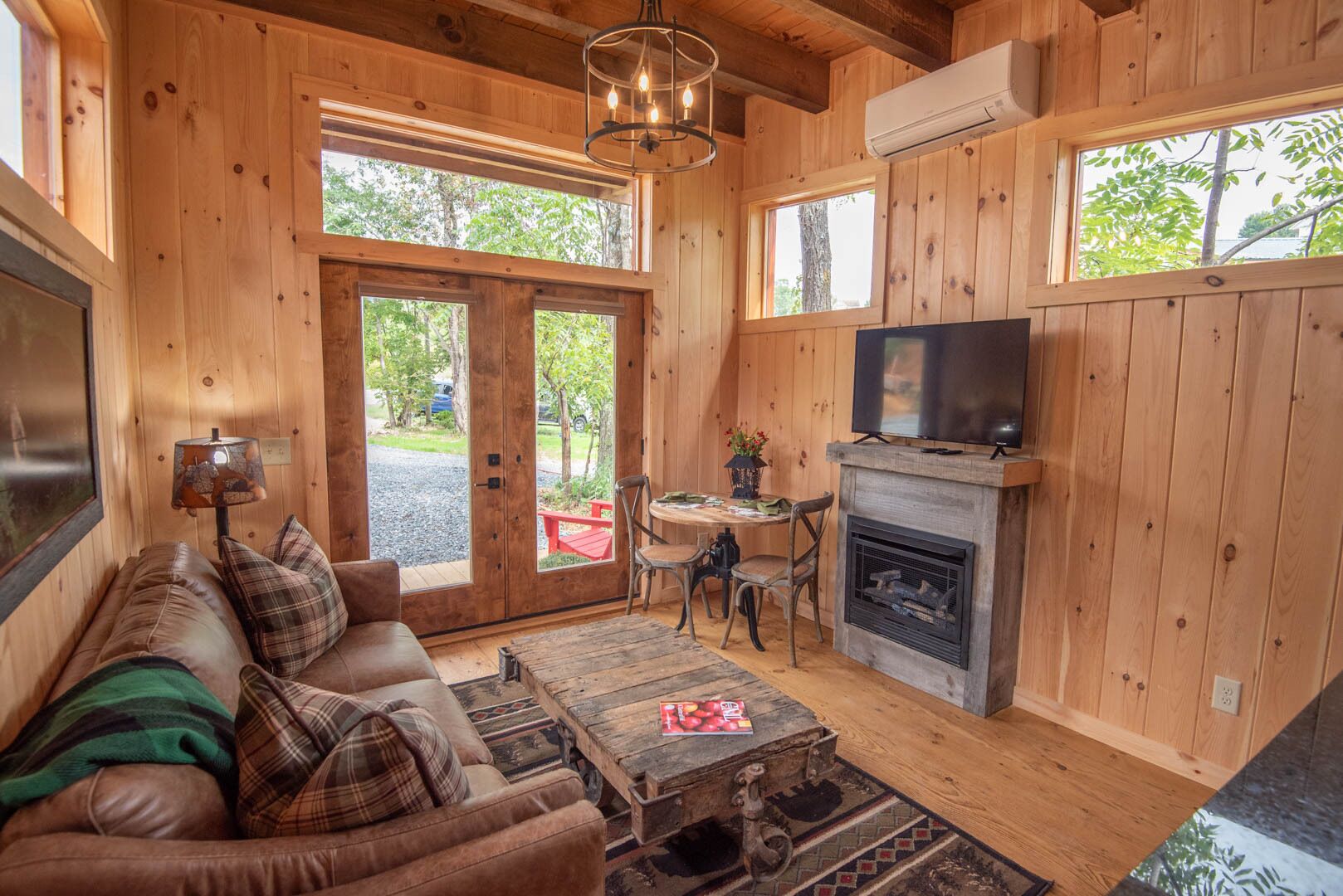 A cozy cabin interior with a leather sofa, a fireplace, a television, and a dining area.
