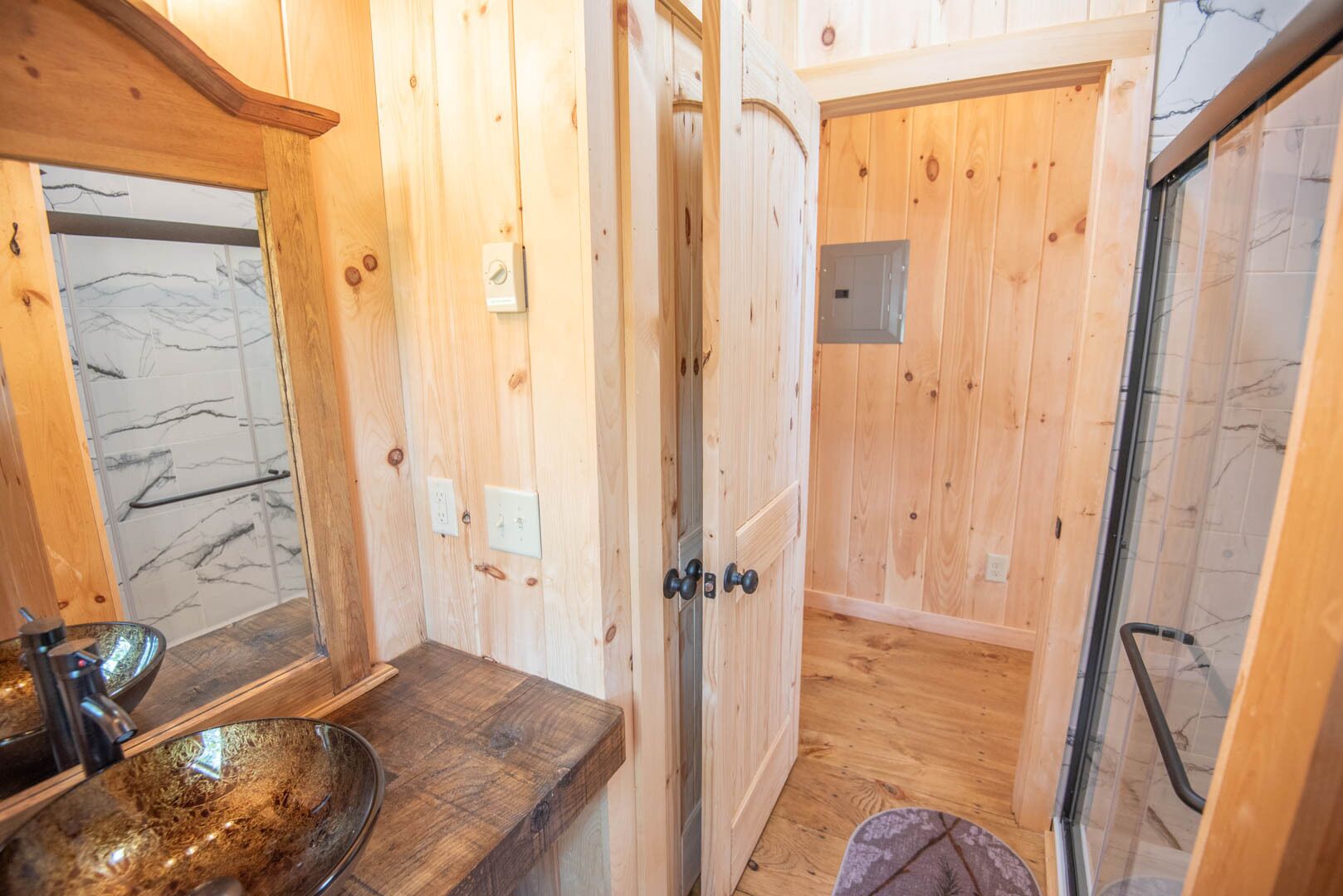 A wooden bathroom with a glass shower enclosure, a marble-tiled wall, and a wooden countertop with a bowl sink.