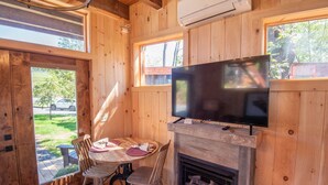 Ein Holzblockhaus-Interieur mit einem an der Wand befestigten Fernseher, einem Kamin und einem Esstisch mit Stühlen.