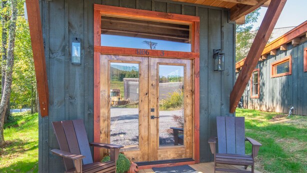 Eine Holzhütte mit einer großen Glasschiebetür, zwei Adirondack-Stühlen und einer Terrasse.