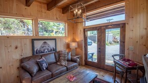 A cozy cabin interior with a wooden interior, a leather sofa, a wooden coffee table, and a large window overlooking a scenic outdoor area.