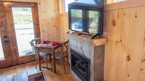 A cozy room with wooden walls, a fireplace, a television on a mantel, and a table with chairs.
