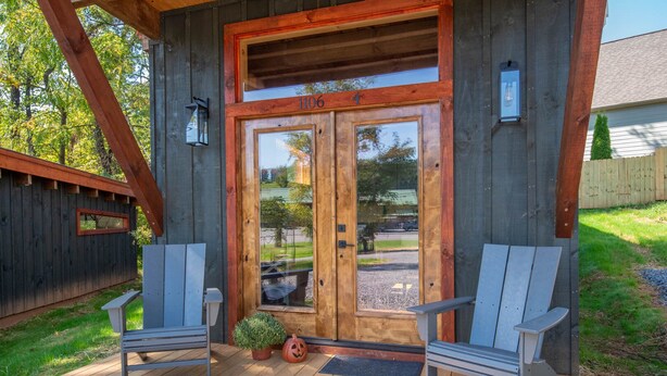 A wooden cabin with a porch, two Adirondack chairs, a mailbox, and a mailbox slot.