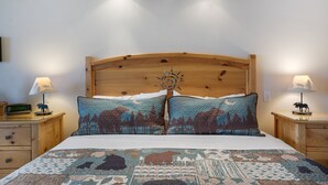 A bed with a wooden headboard, two bedside tables with lamps, and a quilt with animal prints. - Flathead Lake Waterfront Studio! (Bigfork)