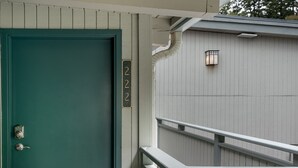 A teal door with a numeric keypad lock, a small window with a light, and a white railing.