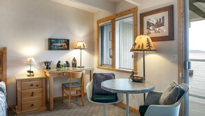 A cozy room with a wooden desk, two chairs, a small table, and a window with a view.