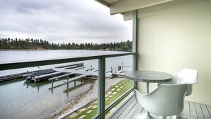A balcony with a view of a lake, a dock, and a table with chairs.