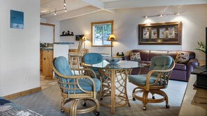 Ein Wohnzimmer mit einem Glastisch, umgeben von Korbstühlen, einem braunen Ledersofa und einem gerahmten Bild über dem Sofa.