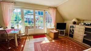A cozy living room with a dining area, large windows, a flat-screen TV, and a wooden cabinet.