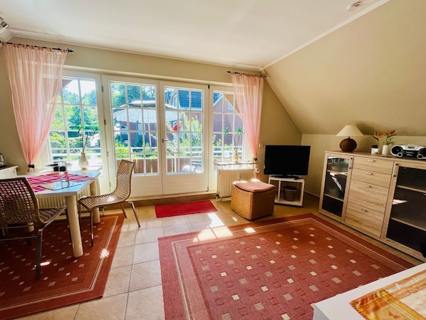 A cozy living room with a dining area, large windows, a flat-screen TV, and a wooden cabinet.