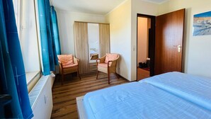 A hotel room with a bed, a chair, a wardrobe, and a window with curtains.