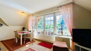 A cozy room with a dining table, chairs, a TV, and large windows with curtains.