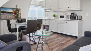 Een moderne keuken met witte kasten, een eethoek met een glazen tafel en uitzicht op zee.