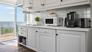 Een moderne keuken met witte kastjes, een magnetron, een koffiezetapparaat en een kamerplant.