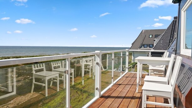 Een houten terras met witte stoelen met uitzicht op de kust.