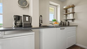 Une cuisine moderne équipée d’une machine à café, d’une bouilloire et d’un évier. Il y a une horloge au mur et une fenêtre avec vue.