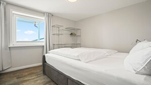 Une chambre avec un lit, une fenêtre avec des rideaux et une étagère métallique adossée au mur.