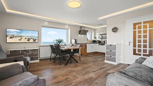 A modern living room with a dining area, a kitchen, and a large window offering a view of the beach. - Käpitäns-suite - Haus Seeblick (Hörnum (Sylt))