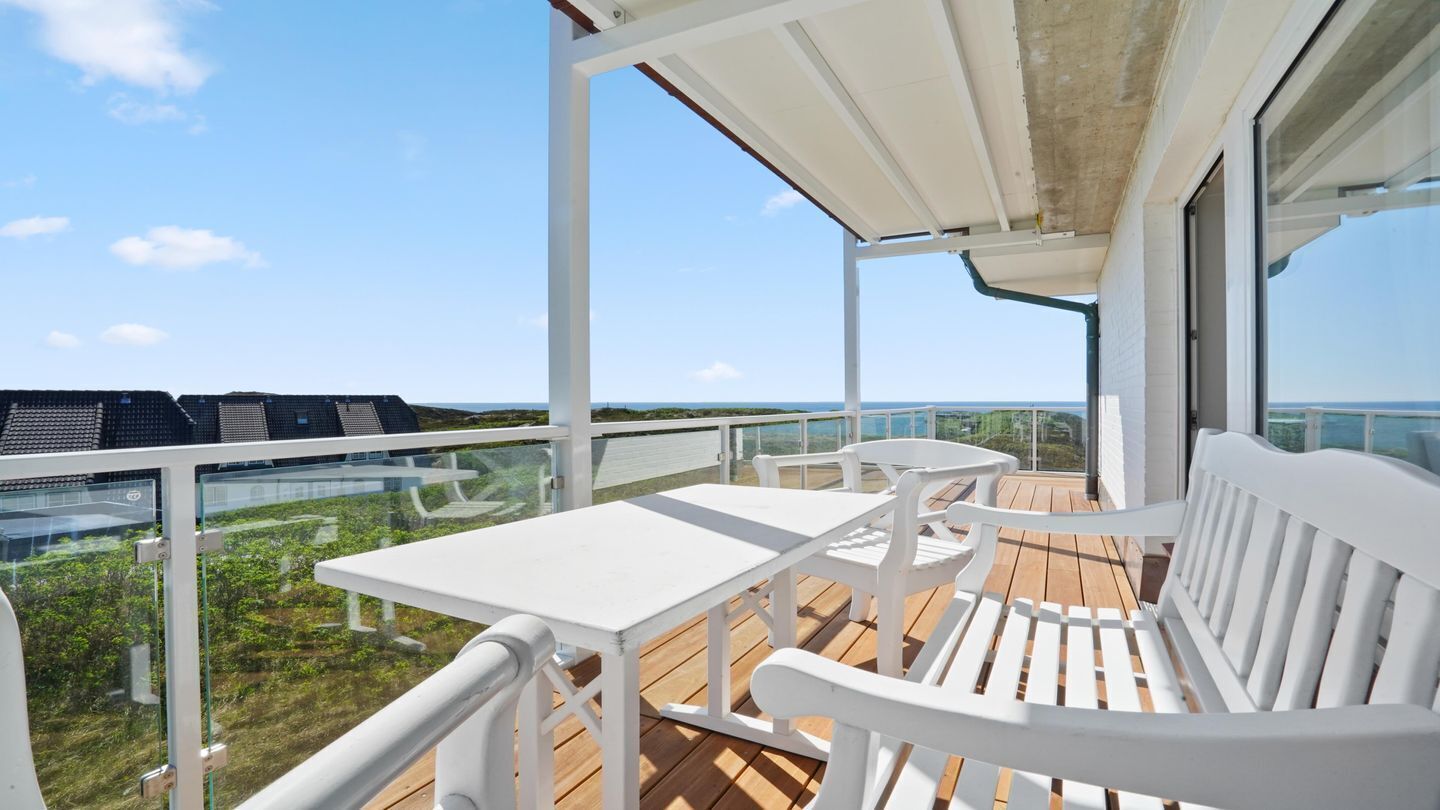 Ein Balkon mit weißen Möbeln, einer Glastrennwand und Blick auf den Ozean.