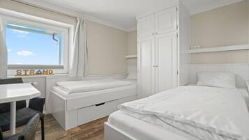 A bedroom with a bed, a desk, and a chair. There is a window with curtains and a sign that reads "STRAND".