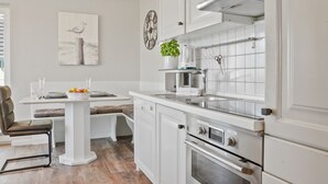 A modern kitchen with white cabinetry, a built-in oven, and a coffee maker. - Meerluft-suite - Haus Seeblick (Hörnum (Sylt))
