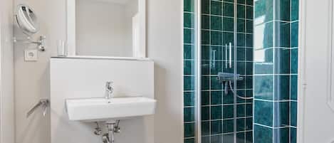 A bathroom with a white sink, a mirror, and a shower with green tiles.