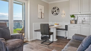 A modern kitchen with white cabinetry, a dining area with a bench, and a view through a sliding glass door. - Meerluft-suite - Haus Seeblick (Hörnum (Sylt))