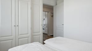 A bedroom with a bed, white walls, and a door leading to a kitchen area. - Meerluft-suite - Haus Seeblick (Hörnum (Sylt))